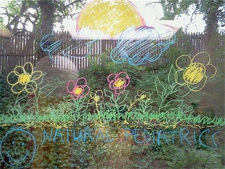 A child's chalk drawing of a sun, clouds and flowers over a garden, with the words Natural Pediatrics written underneath.