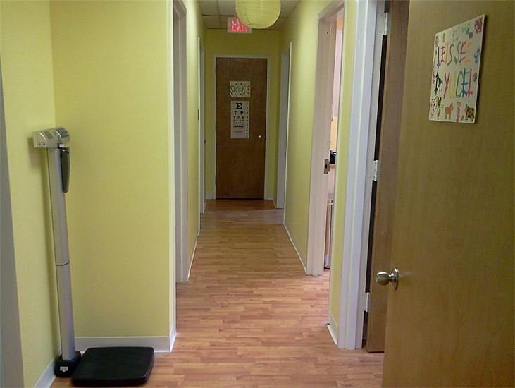The hallway between exam rooms, painted pale green, with a scale and an eye chart on the far door.
